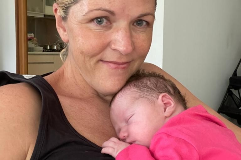 A new mum smiles while her newborn daughter sleeps on her chest