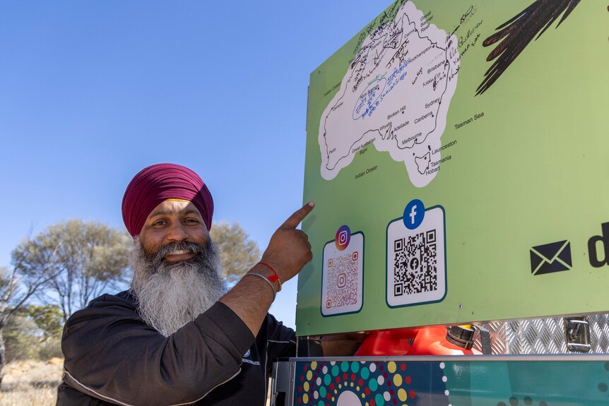 A man in a turban stands pointing at a map of Australia on a van. 