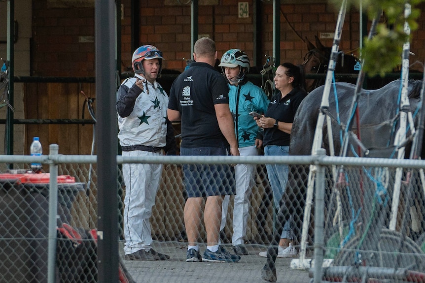 A man in a black shirt speaks to two horse drivers.