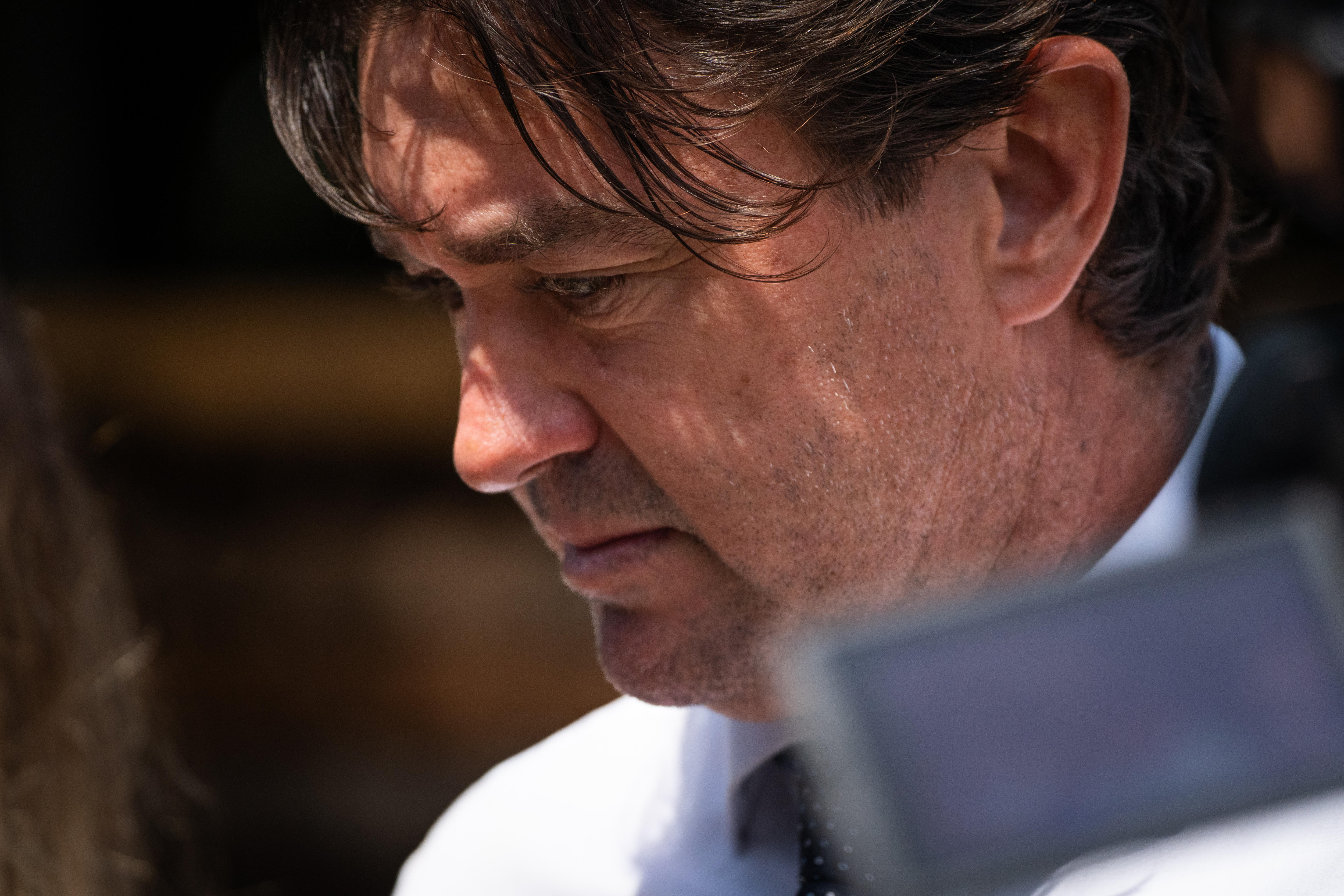 A close-up of a man with dark hair, looking towards the ground.