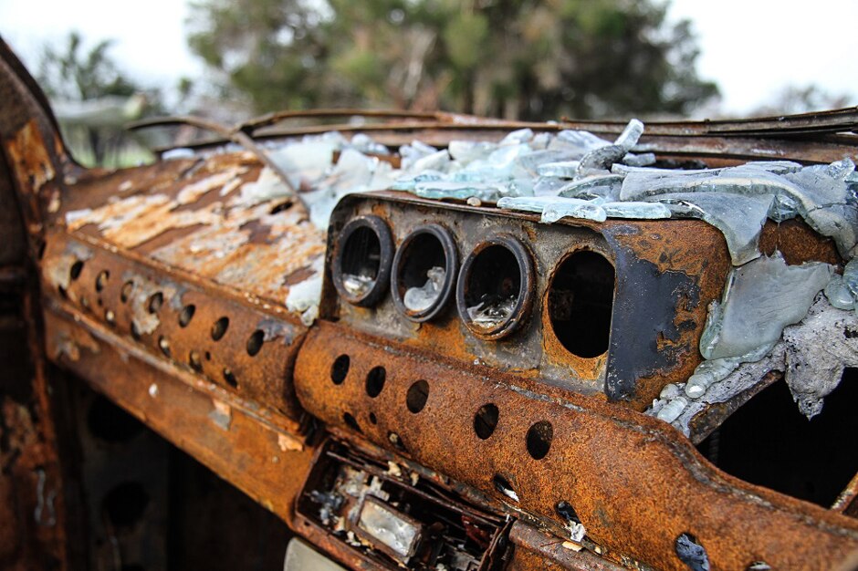 Rusted burned out dashboard covered in melted windscreen glass.