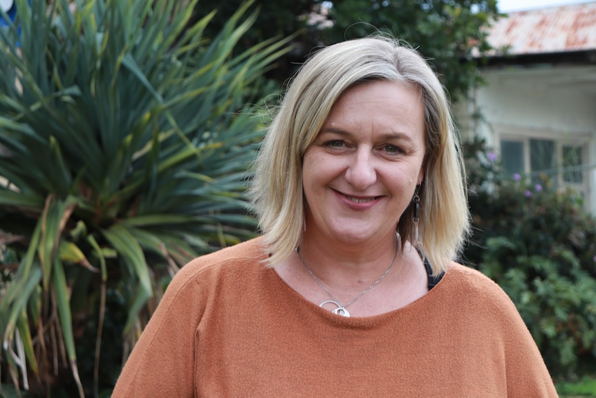 Lady wearing orange top smiling.