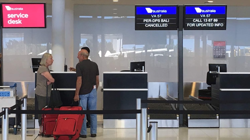 A couple at a check-in counter at Perth Airport where a sign tells of flight cancellations to Bali.