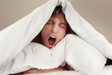 Young man with pillow under quilt yawning