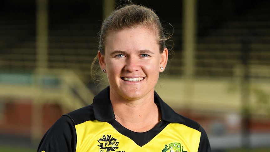Jess Jonassen stands in her yellow cricket shirt smiling at the camera