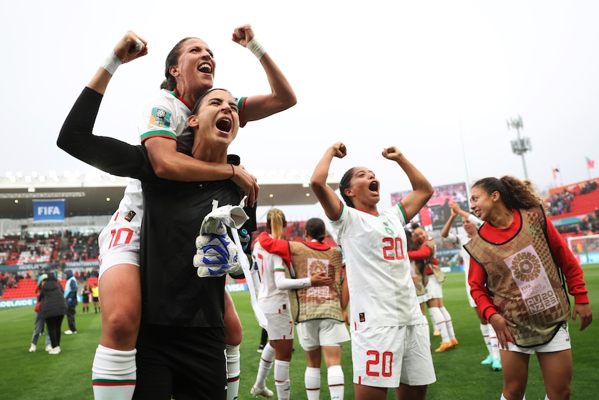 A goalkeeper and several players for Morocco pump their fists in celebration at the crowd after a win at the Women's World Cup.