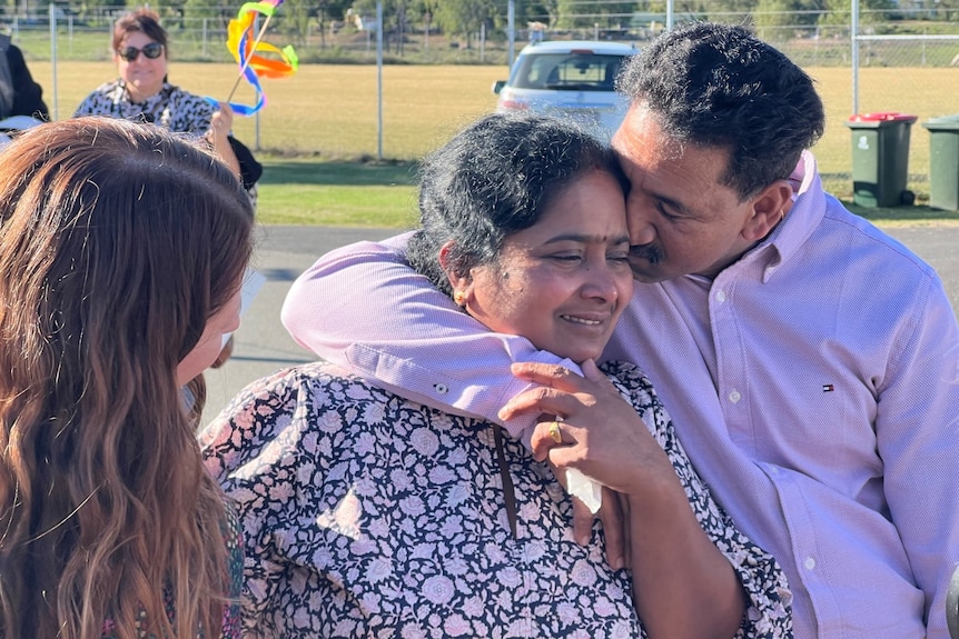 A husband kisses his wife on the tarmac at an airport.