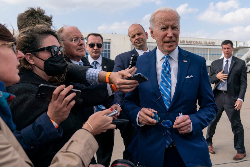 Joe Biden holds his sunglasses and reporters hold out recorders