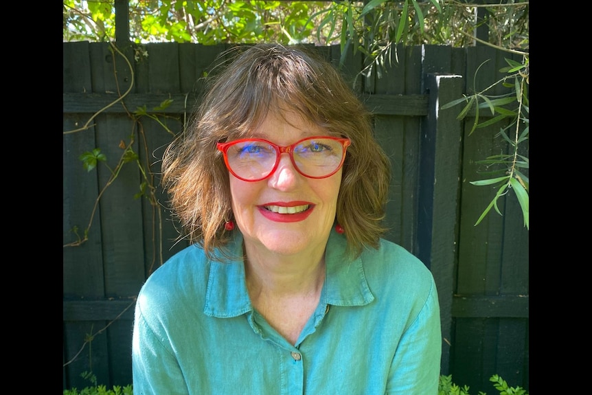 A woman wearing glasses and a green shirt looks directly at the camera