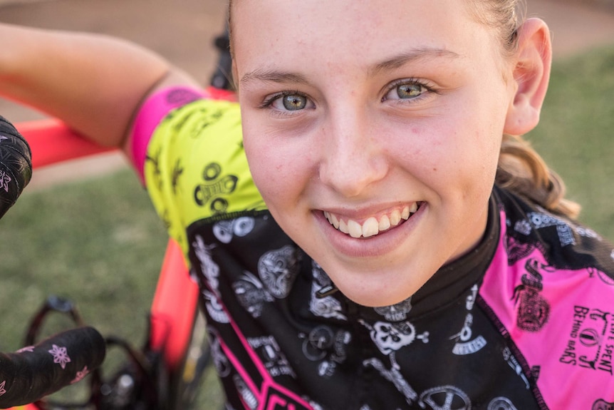 A young girl leaning on a bicycle smiles at the camera.