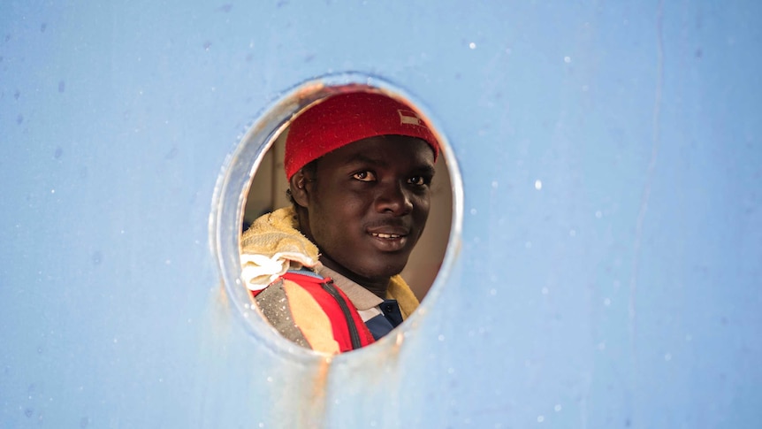 A man smiles through the porthole from aboard the Sea-Eye ship.