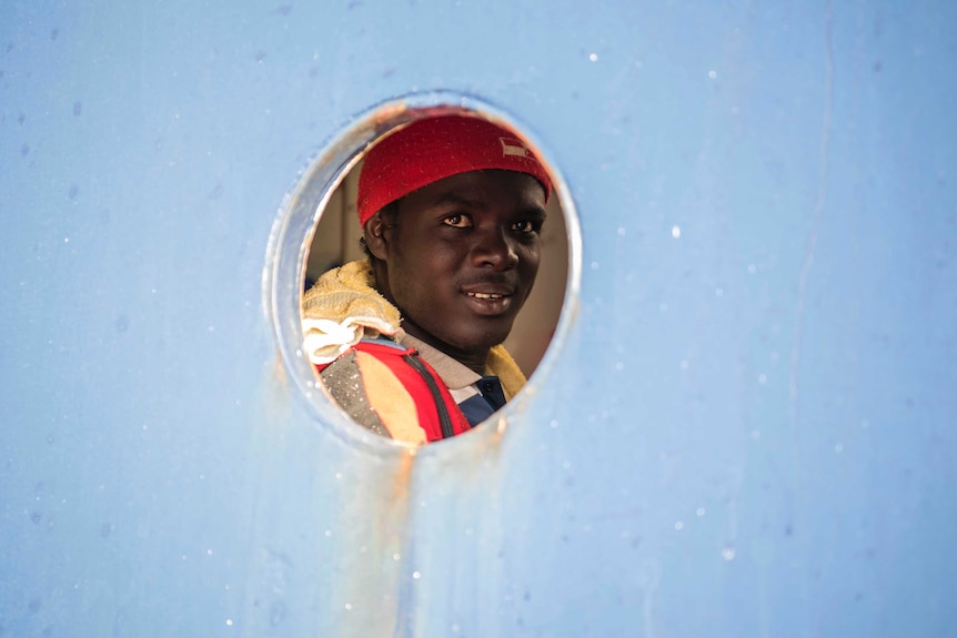 A man smiles through the porthole from aboard the Sea-Eye ship.