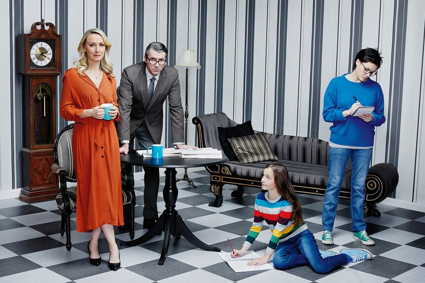 Three people and a young girl pose in a stylised living room theatre set with wallpaper and black and white chequered floor.