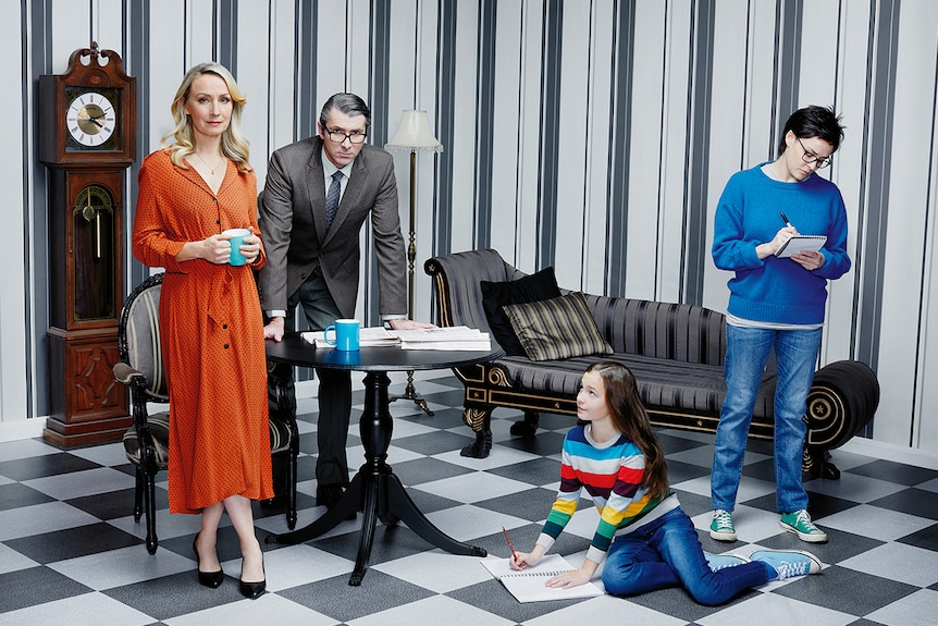 Three people and a young girl pose in a stylised living room theatre set with wallpaper and black and white chequered floor.