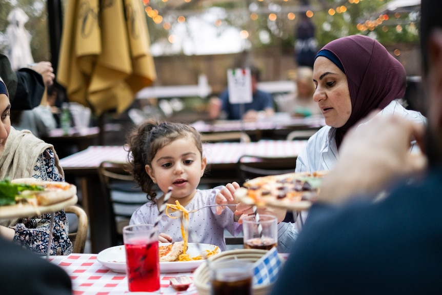 a woman and a child sit at an outdoor table eating 