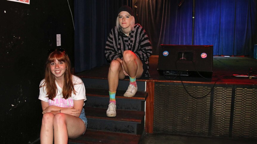 Two young women sit on some steps leading up to a stage.