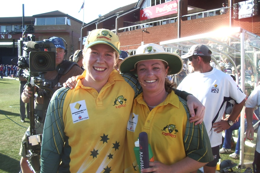 Two women look at the camera with their arms around each other, smiling.