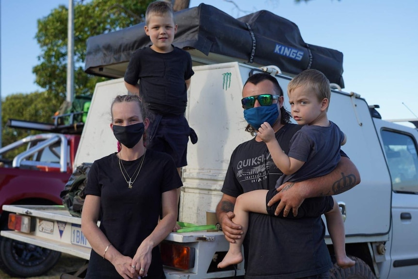 A mum and dad with their two children and their packed up car in the background