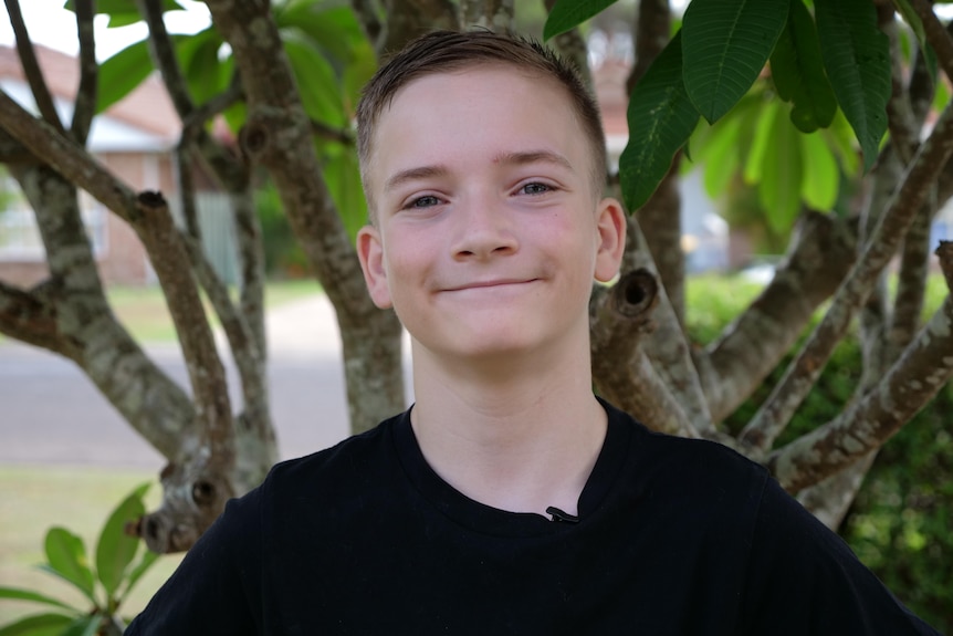Portrait of a 13 year old boy smiling in front of a tree