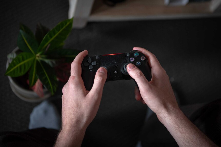A man's hands hold a PlayStation controller.