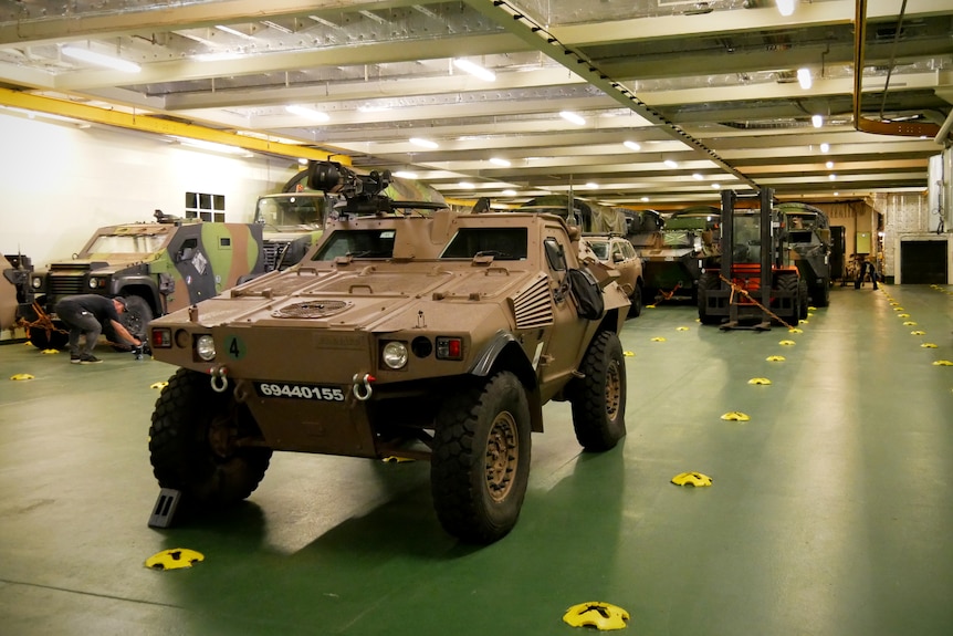 Numerous armoured personnel carriers park inside a ship