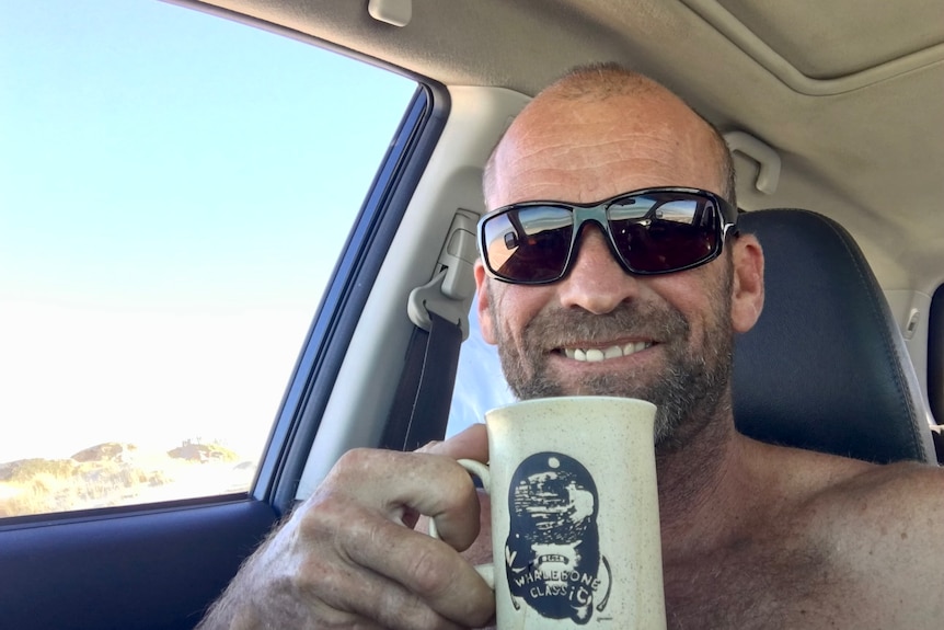 Selfie of man in sunglasses smiling with coffee cup.