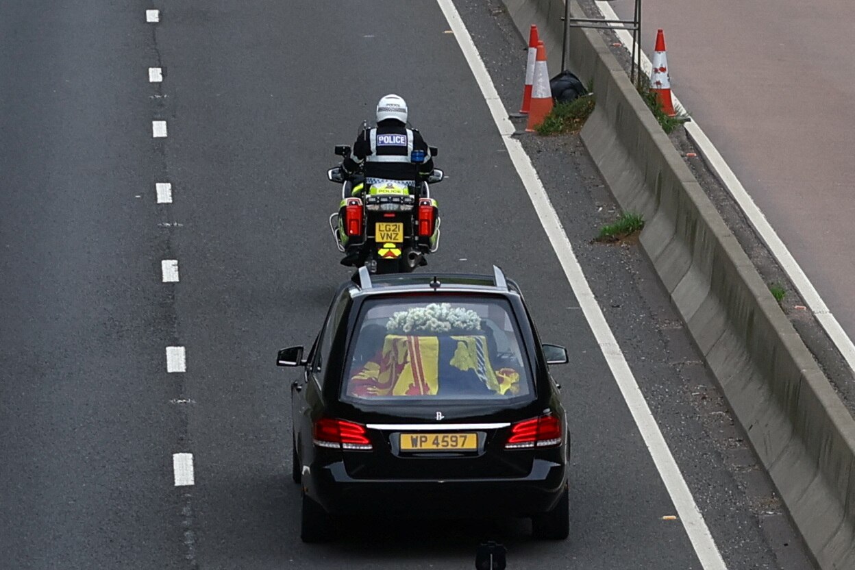 Hearse carrying the Queen's coffin follows a motorbike police officer on a motorway. 