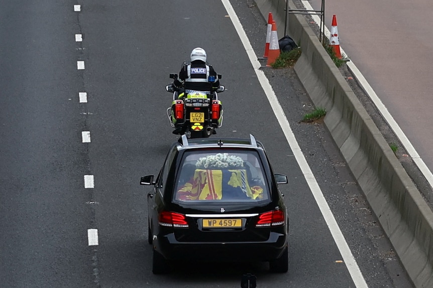 Hearse carrying the Queen's coffin follows a motorbike police officer on a motorway. 