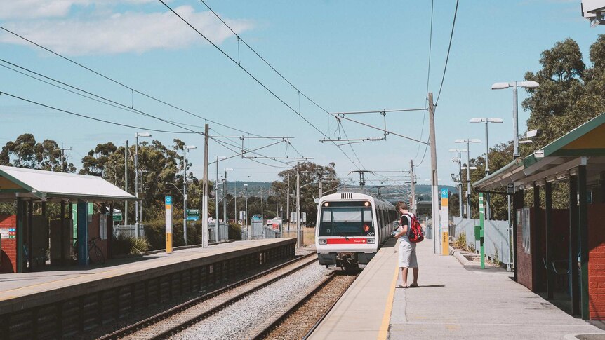 A train pulls into Seaforth Station in Gosnells with a passenger standing on the platform waiting.