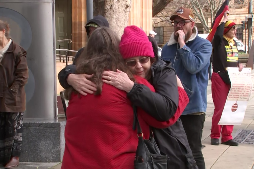 two people hug while other people with signs in the background