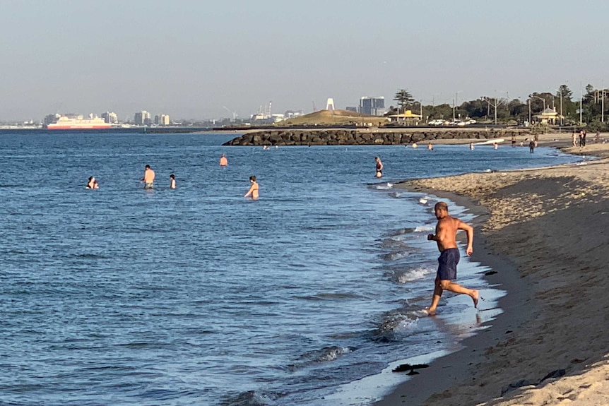 A man in dark blue shorts runs into the water in early morning light at a bayside beach.