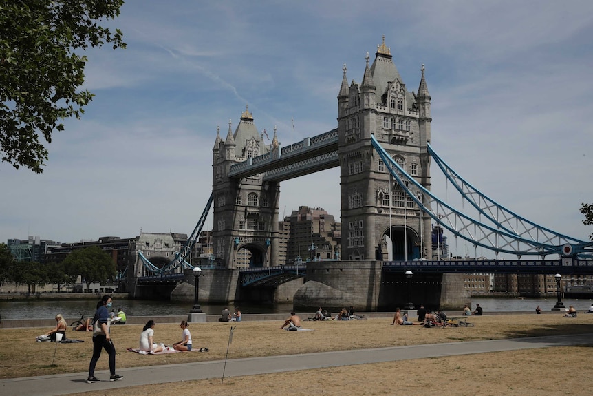 People relax in the sun backdropped by Tower Bridge, at Potters Fields Park by the River Thames in London, UK