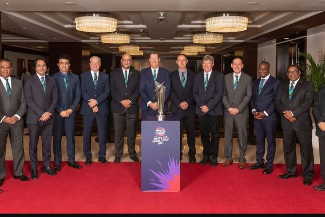 A group of male international cricket executives stand in a row in front of the ICC Men's T20 World Cup trophy