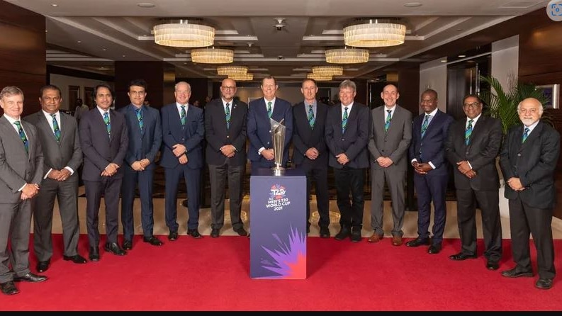 A group of male international cricket executives stand in a row in front of the ICC Men's T20 World Cup trophy