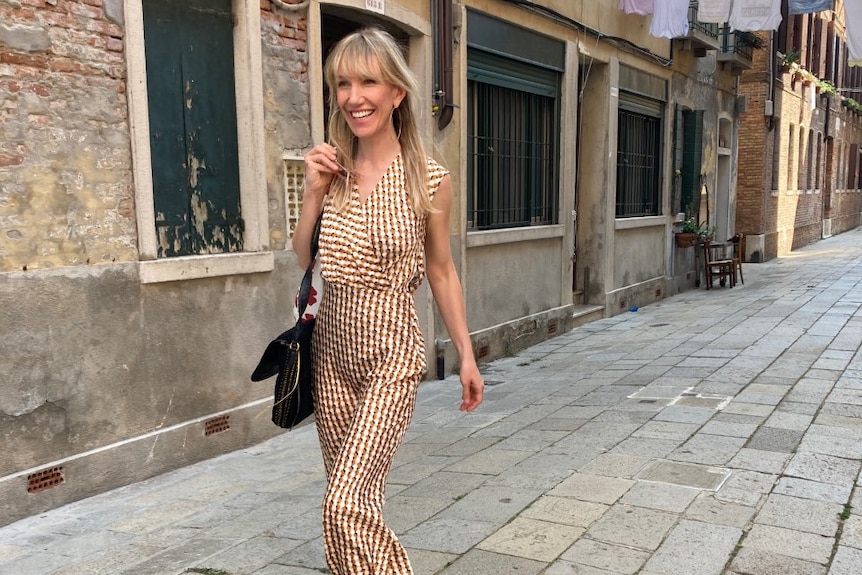 A smiling woman walking down a street in Venice. 