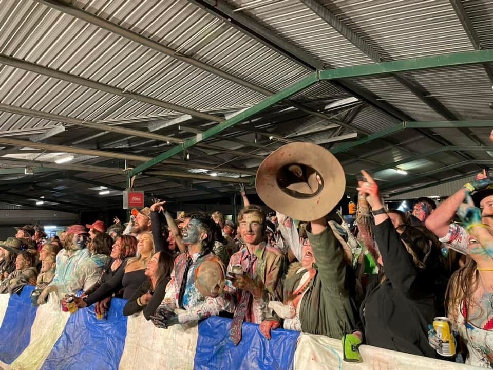 A group of you people covered in food dye watching a band on stage