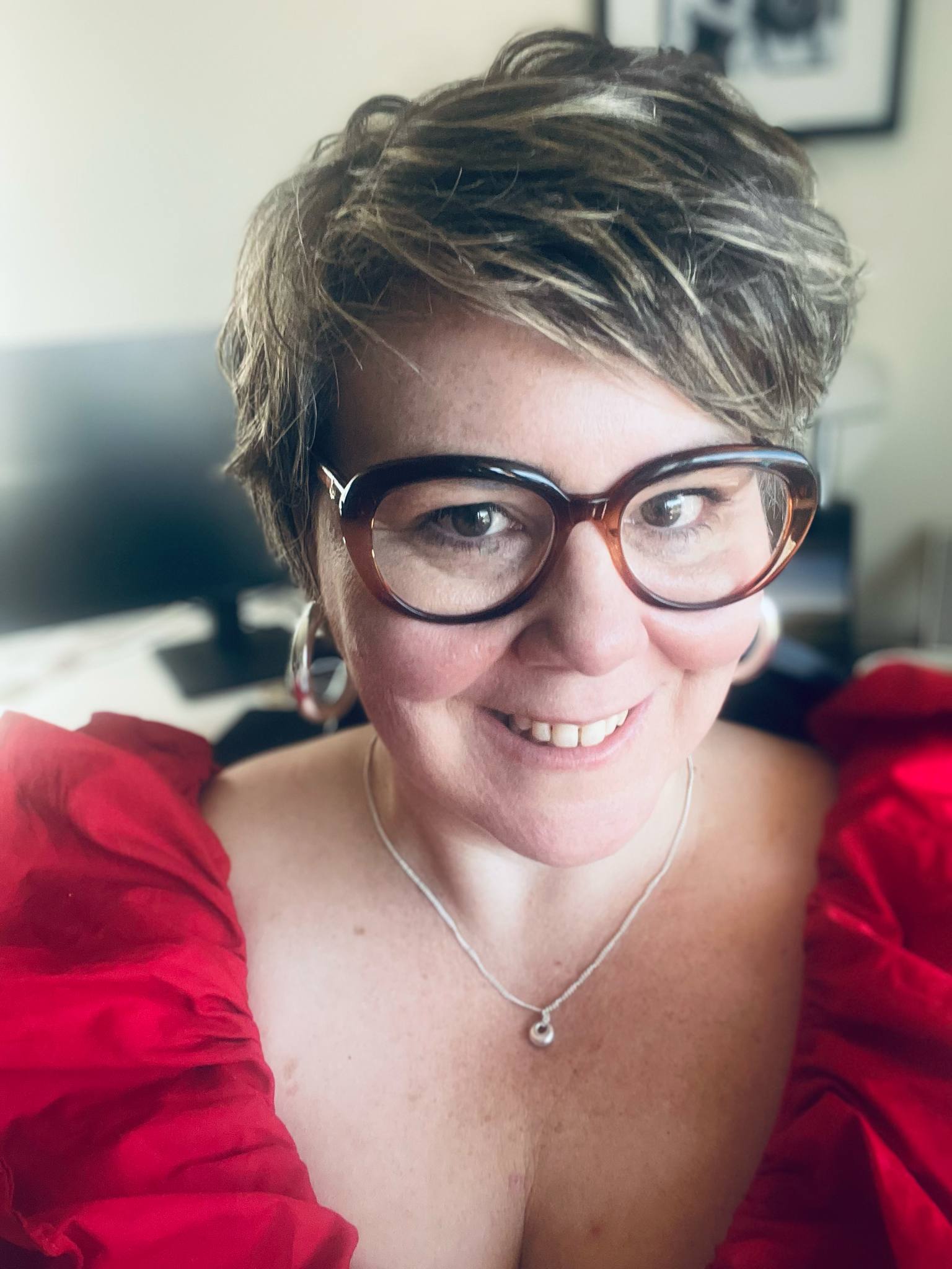 A woman with glasses and curly hair smiling for the camera for a selfie