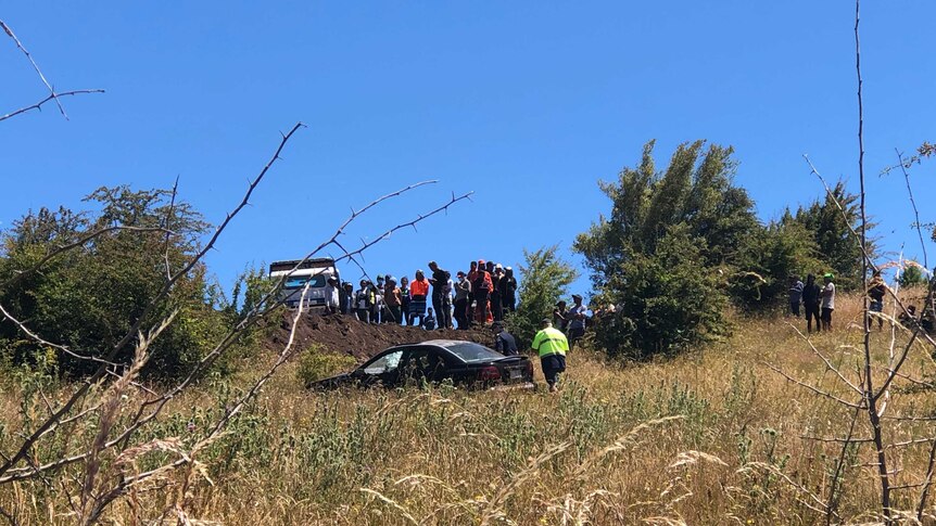 A group of people gather at the site of a car crash, while police attend.