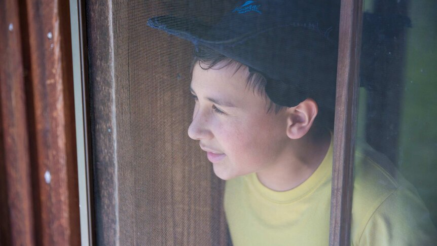 A student squints out from a wooden window frame into the glare.