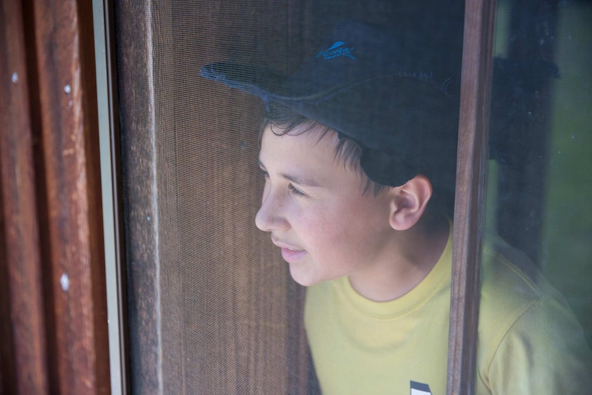 A student squints out from a wooden window frame into the glare.