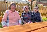 The elderly Indigenous women sitting at a table outside.