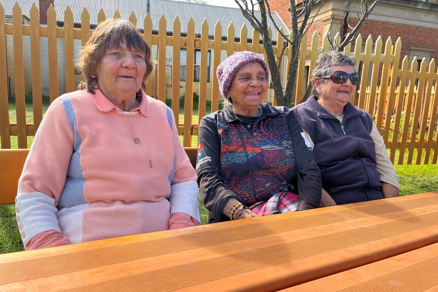 The elderly Indigenous women sitting at a table outside.