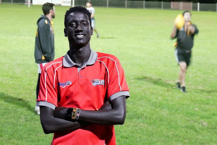 Mach Mach standing in front of a footy field with players practising in the background.