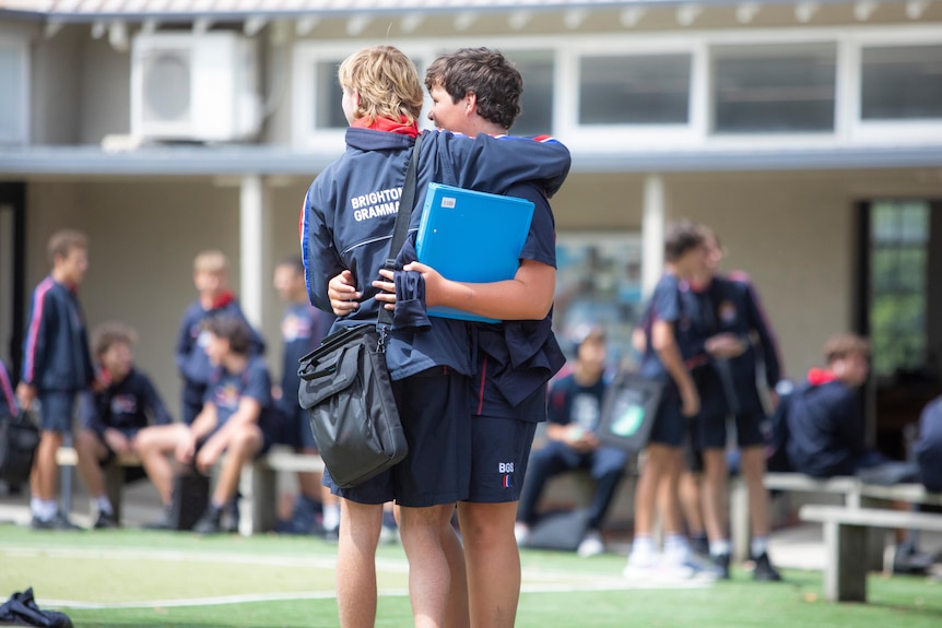 Two male school students with their backs turned, arms around each other and smiling