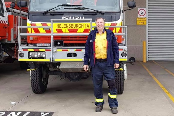 A middle-aged man in a firefighter's uniform stands in front of a fire truck