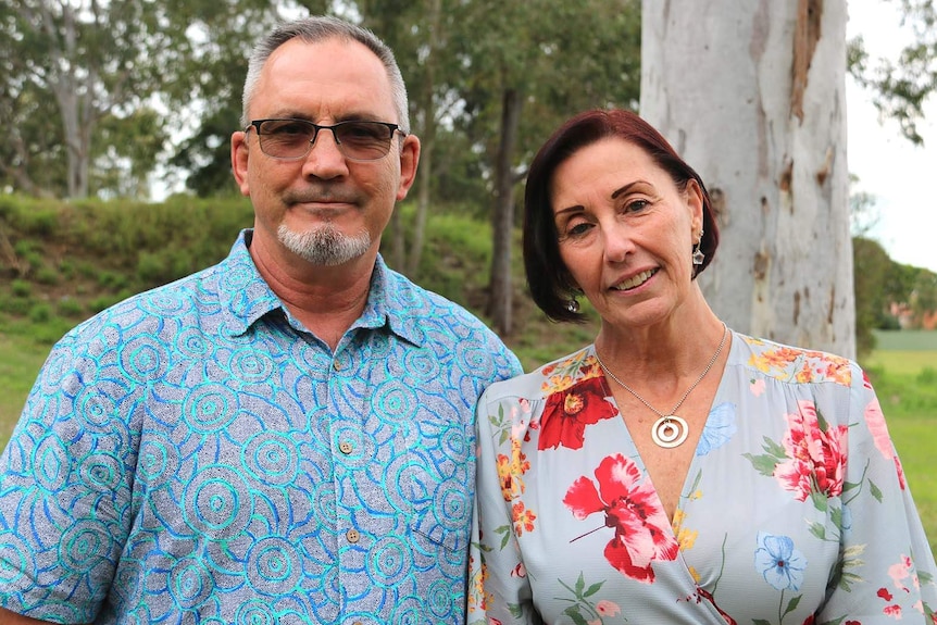 A man and a woman smiling while standing near a tree in a park