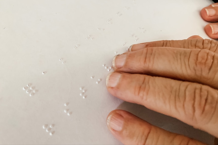 a close up image of a hand on a piece of paper with letters of the Braille alphabet