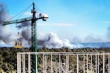 A fire burns in the distance as researchers in a cage suspended by a crane take carbon measurements