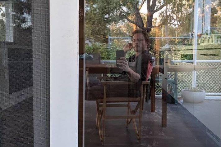 A young man takes a selfie through a window reflection