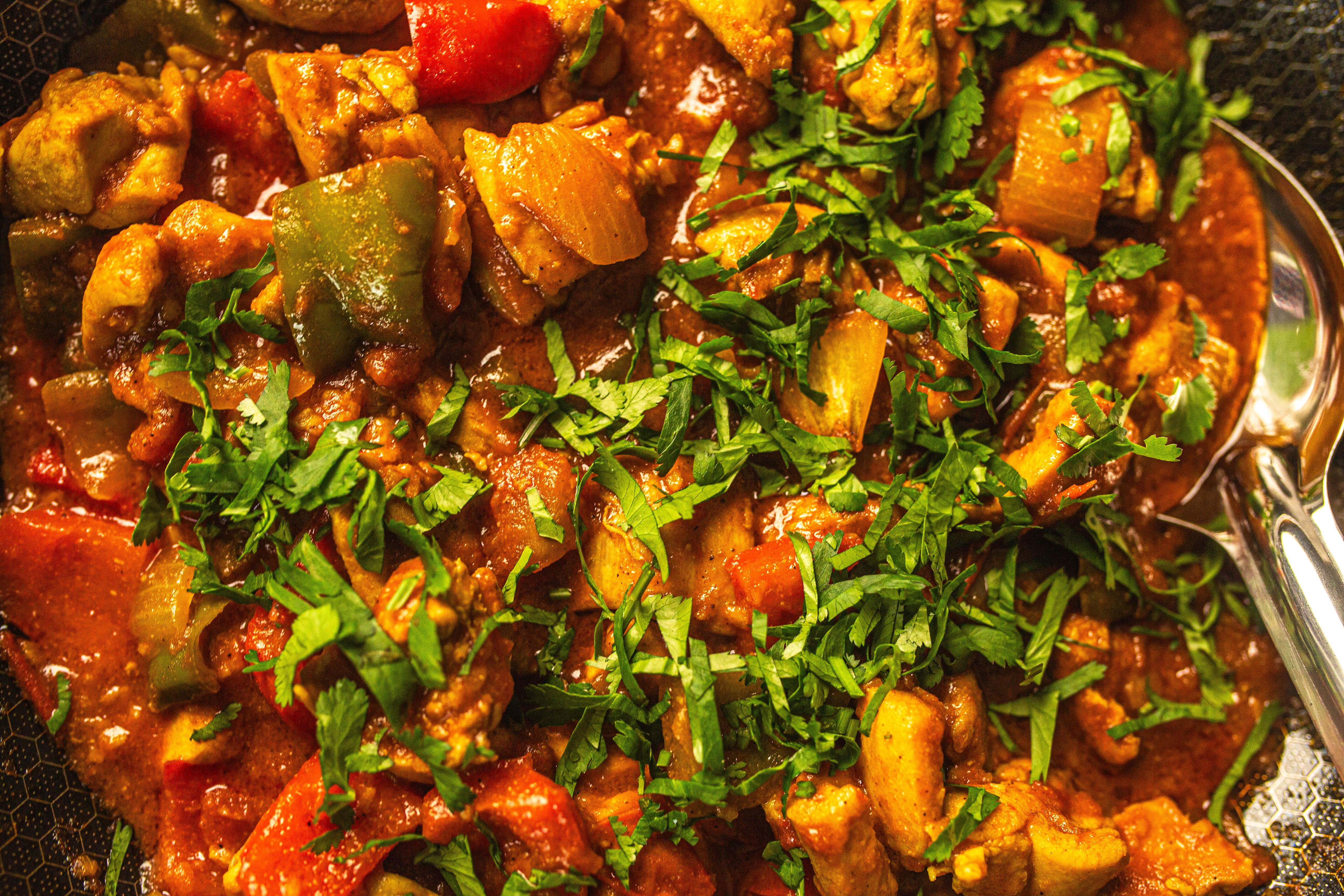 A close up shot of chicken jalfrezi, a tomato-based curry with chicken thighs, onions, capsicums, spices and tinned tomato. A
